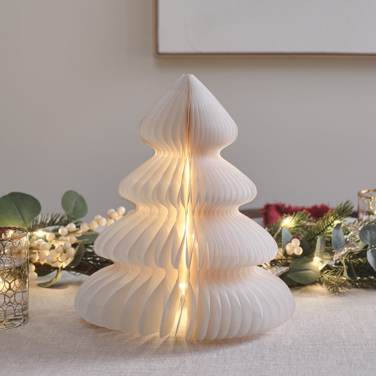 Beleuchteter weißer Papier-Weihnachtsbaum mit warmweißen LEDs auf Tisch mit Deko