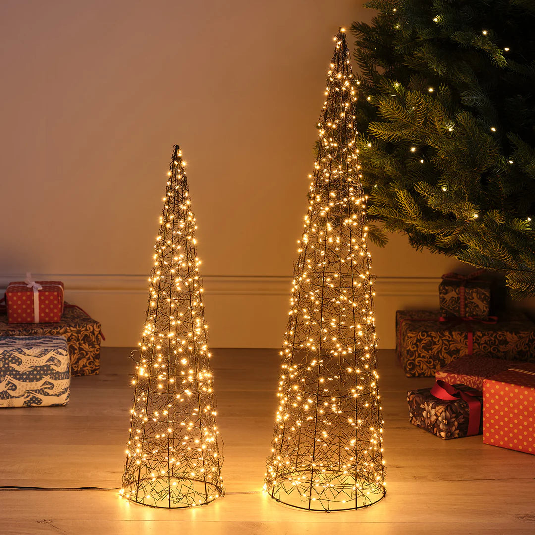 Zwei LED-Drahtkegel in 60 cm und 80 cm Höhe mit warmweißen Lichtern auf Holzboden neben Weihnachtsbaum