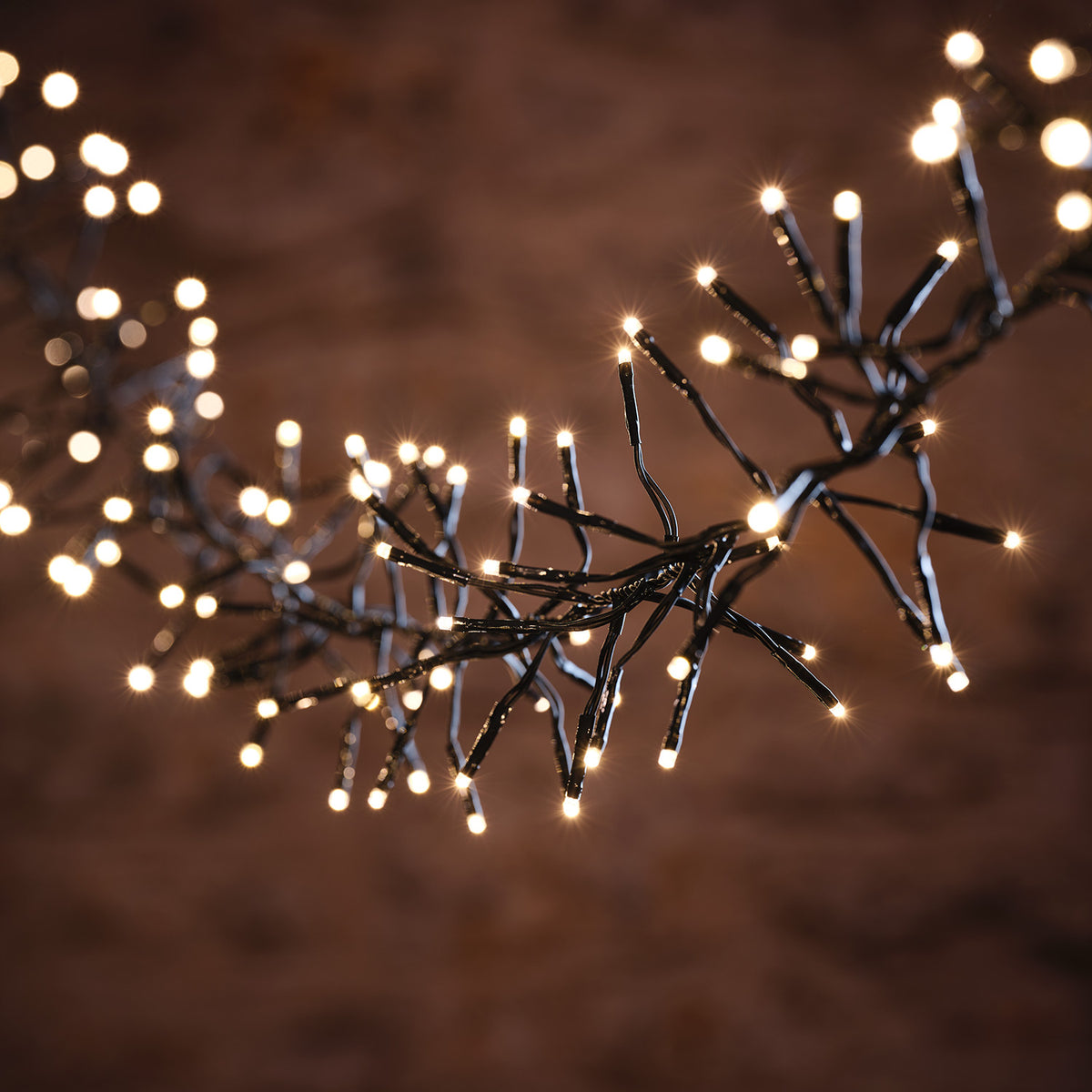 Lichterkette mit warmweißen LEDs auf schwarzem Kabel vor braunem Hintergrund