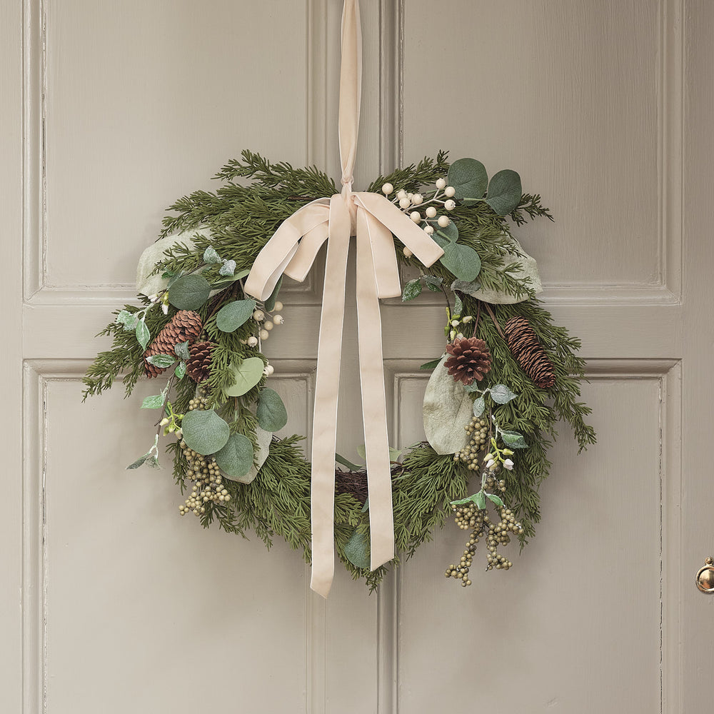Eleganter Weihnachtskranz mit natürlichem Grün, burgunderfarbenen Beeren und weißer Schleife an grauer Haustür.