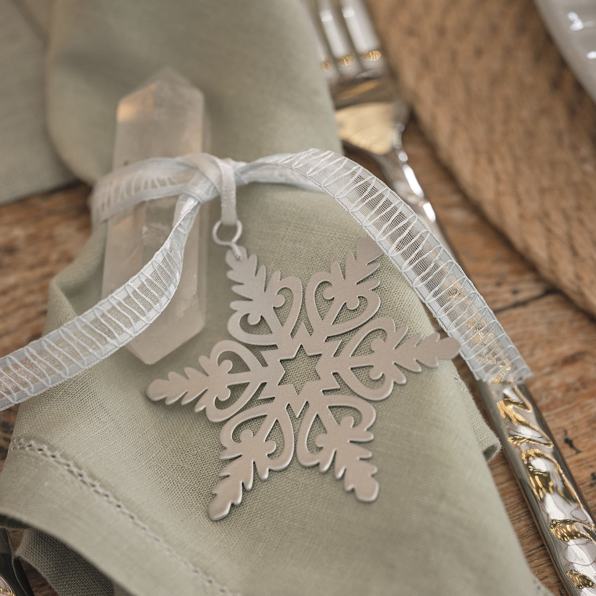 Weißer Schneeflocken-Anhänger als Geschenkanhänger an Serviette mit Schleife.