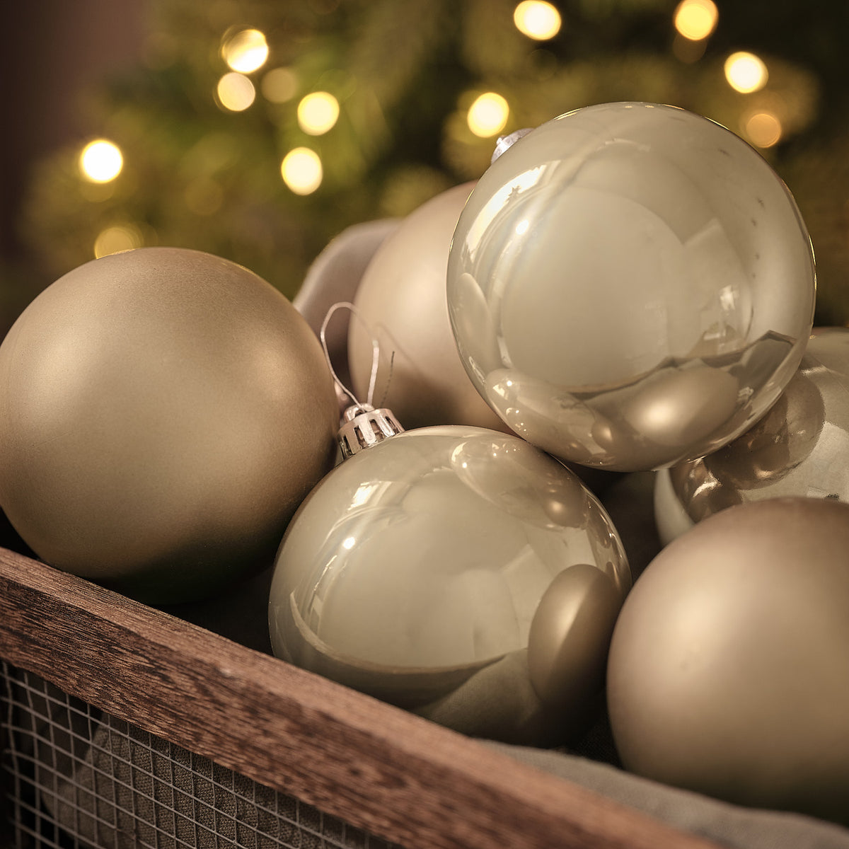 Weihnachtskugeln in matter und glänzender Optik in Holzkiste vor Lichterglanz.