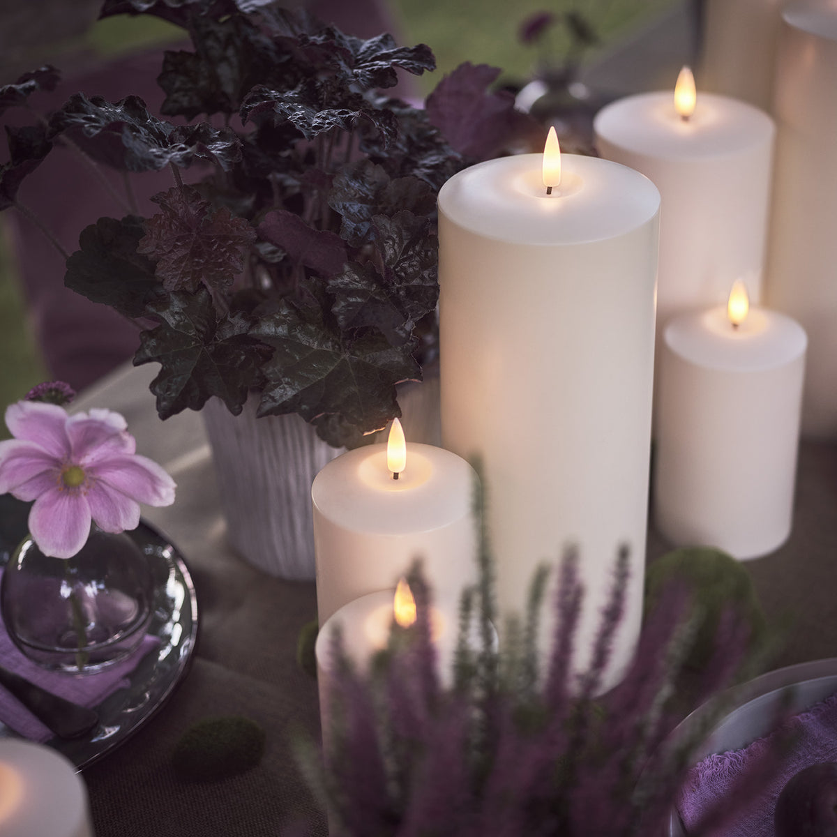 LED-Kerzen mit violetten Pflanzen und gedecktem Tisch mit Obst und Besteck
