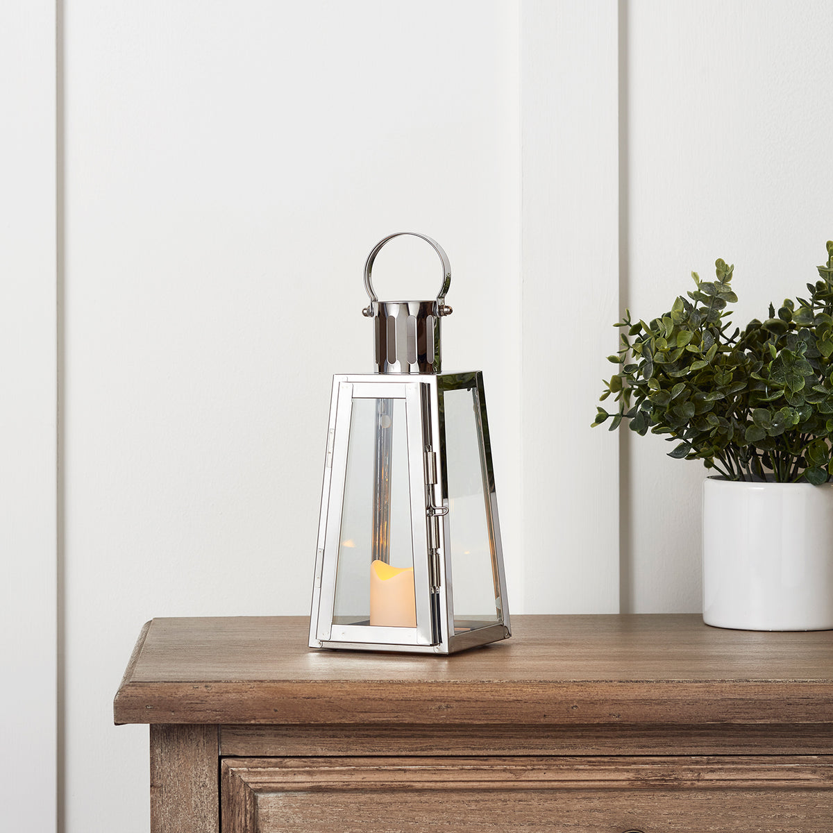Edelstahl LED Laterne mit flackernder Kerze auf Holzkommode neben Pflanze