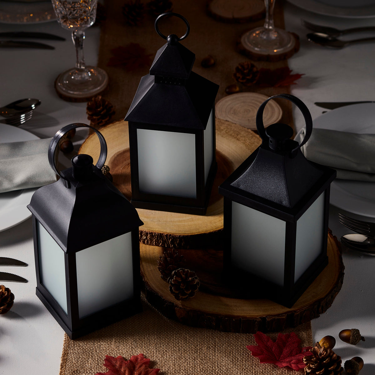 Drei schwarze Gartenlaternen mit ausgeschaltetem Licht auf Holzscheiben mit Herbstdeko