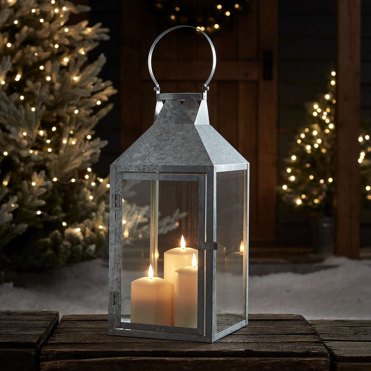 Große verzinkte Laterne mit drei TruGlow LED-Kerzen auf Holztisch mit Lichterkette und Deko