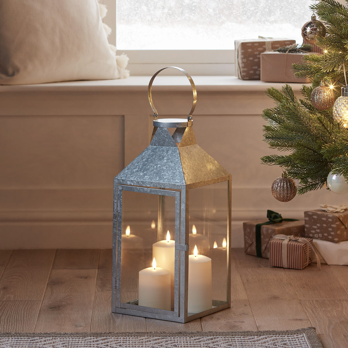 Große verzinkte Laterne mit drei TruGlow LED-Kerzen auf Holzboden neben Weihnachtsdeko und Geschenken