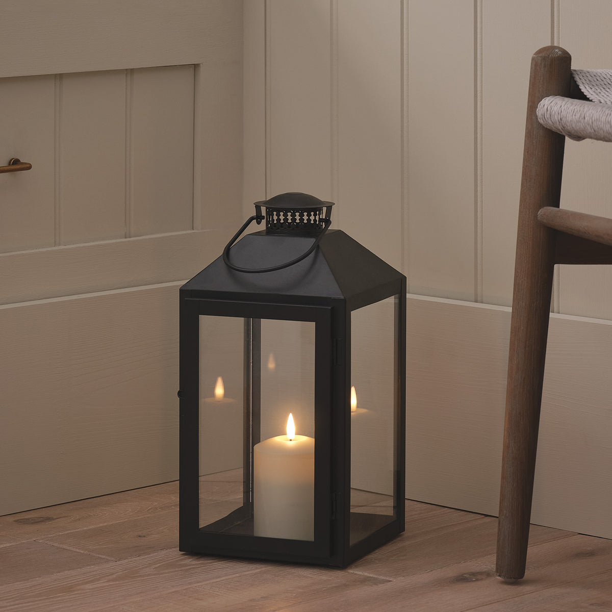 Große schwarze Metalllaterne mit TruGlow LED-Kerze auf Holzboden neben Stuhl