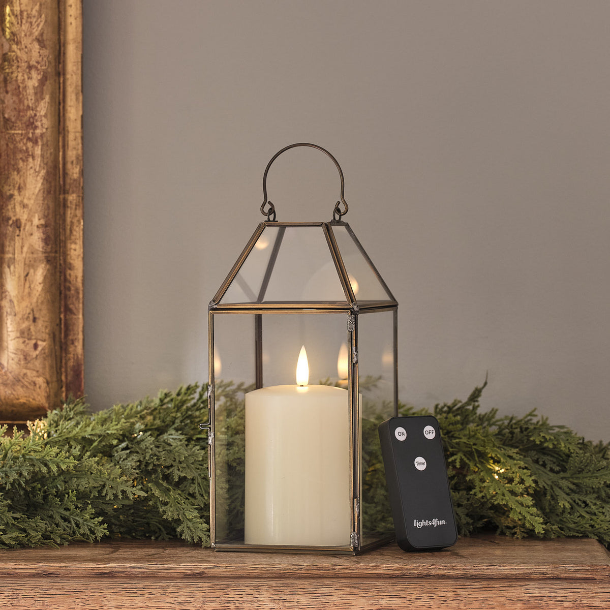 Goldene LED-Laterne mit TruGlow® Kerze und Fernbedienung auf Holz vor grüner Dekoration
