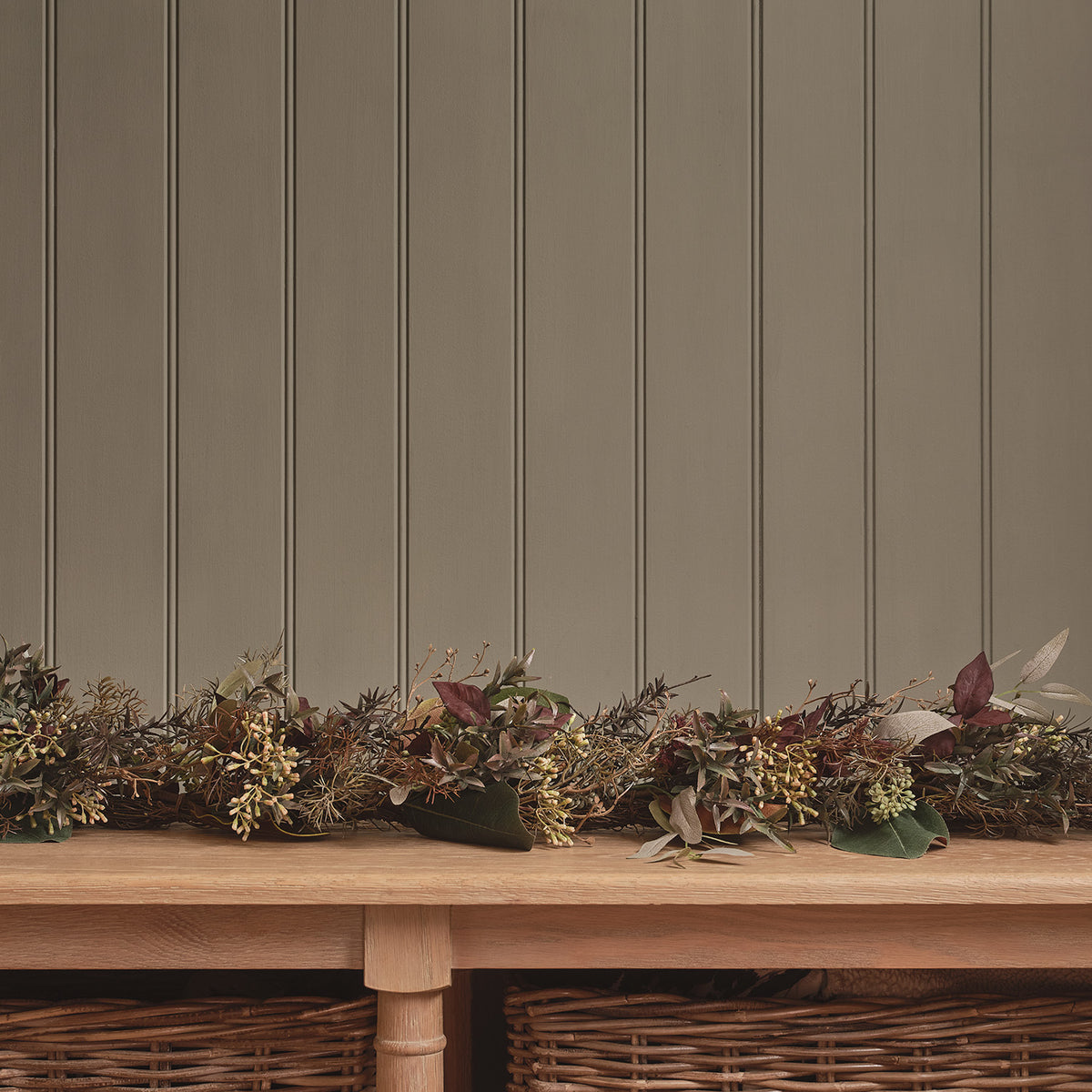 Herbstgirlande mit warmweißen LEDs und buntem Laub auf einem Holztisch vor grauer Wand