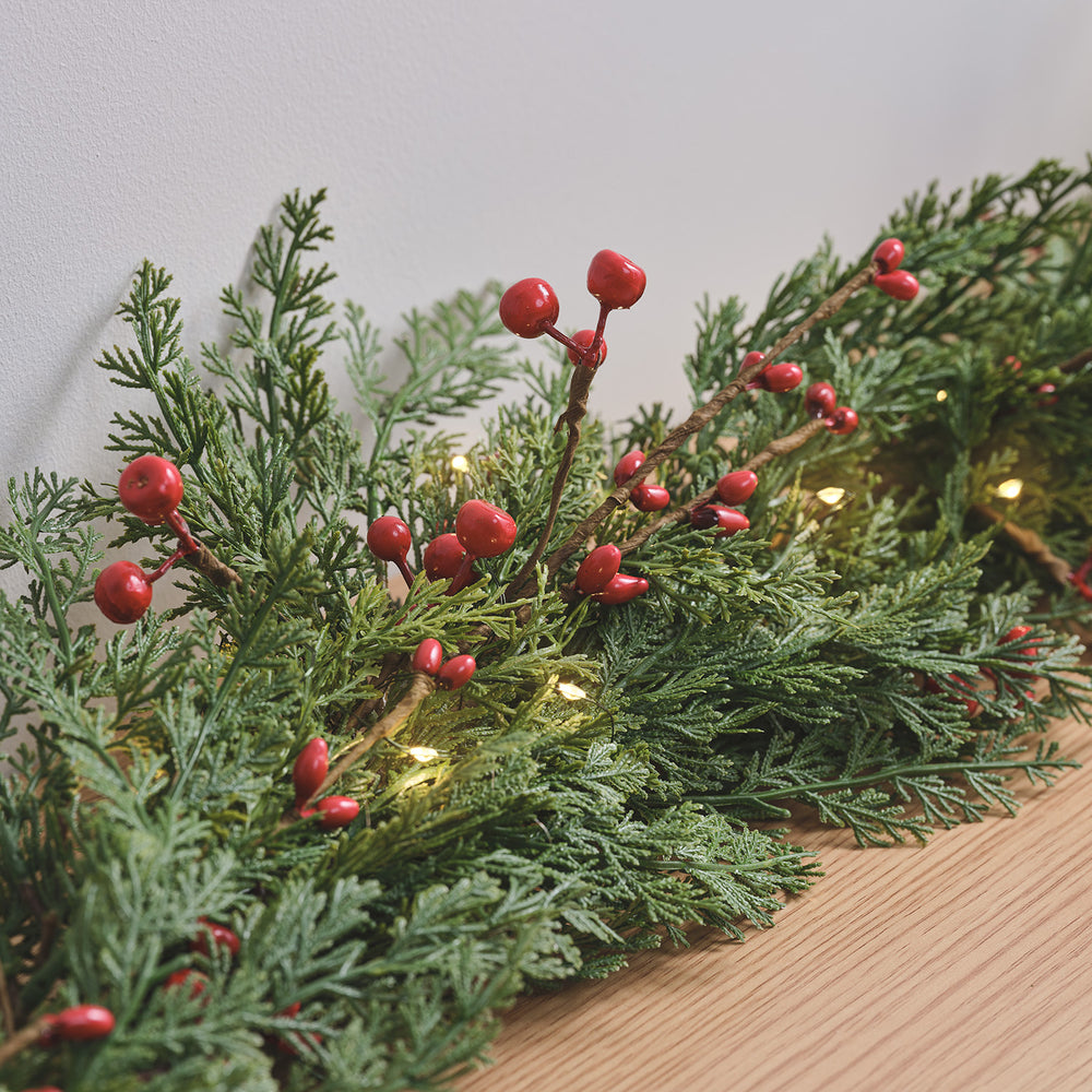Nahaufnahme der Weihnachtsgirlande mit roten Beeren und grünem Kunst-Tannengrün auf Holztisch