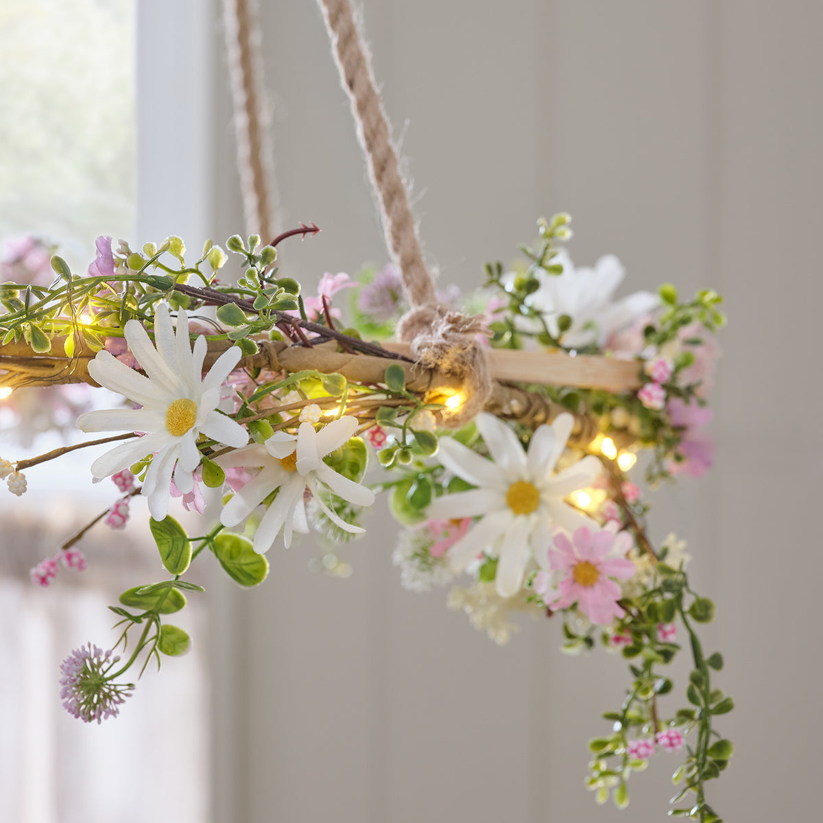 Hängende LED Blumengirlande mit Gänseblümchen und Mikrolichtern vor hellem Fenster