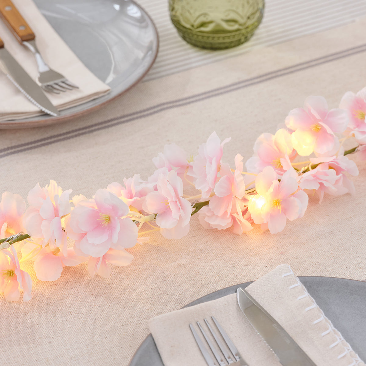 Leuchtende LED-Blumengirlande mit rosa Blüten auf gedecktem Tisch mit Besteck und Serviette