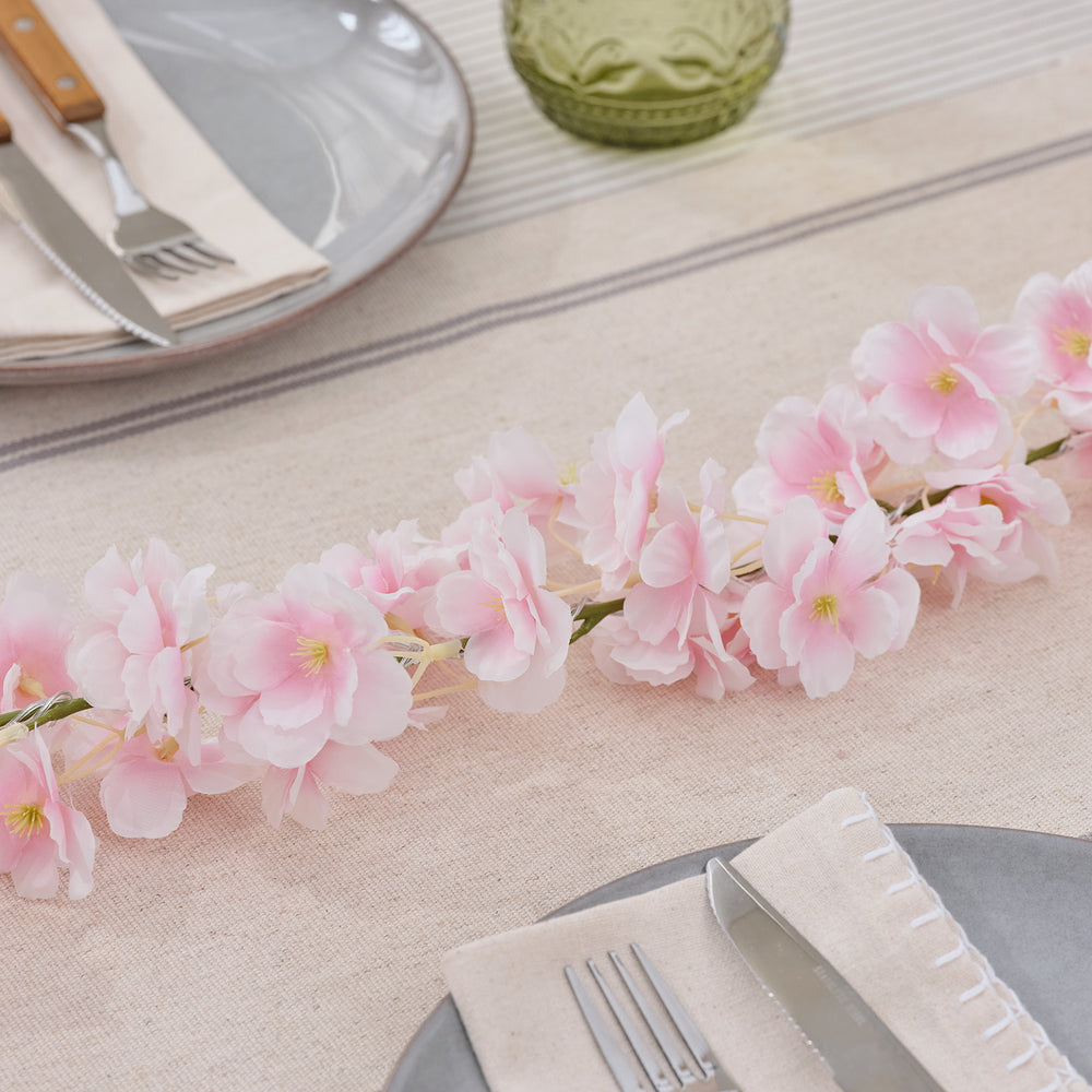 Pastellrosa LED-Blumengirlande dekorativ auf gedecktem Esstisch mit Besteck und Gläsern