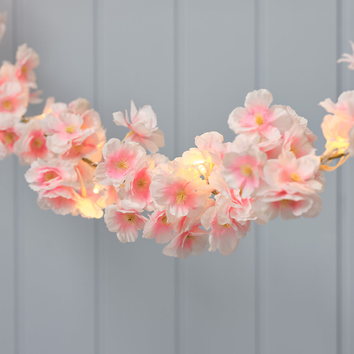LED-Blumengirlande mit pastellrosa Kunstblüten und warmweißen LEDs vor grauer Wand