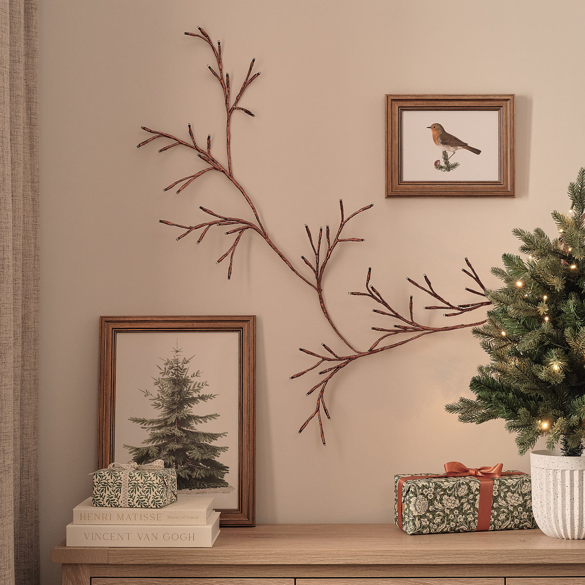 Bronzefarbene LED-Zweiggirlande ohne Beleuchtung an Wand neben Bildern und Tannenbaum