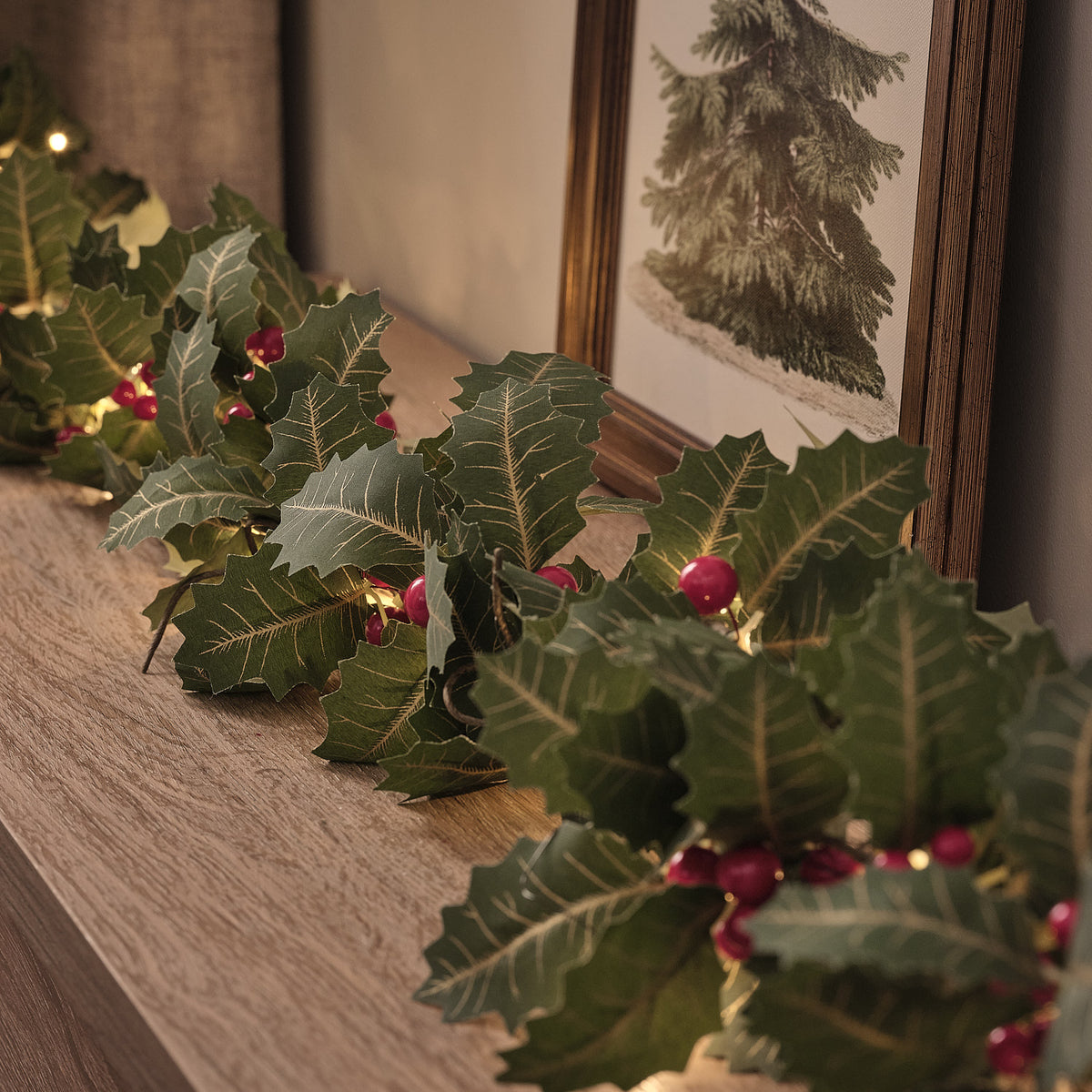Nahaufnahme der Stechpalmen-Girlande mit warmweißen LEDs und roten Beeren auf Holzfläche