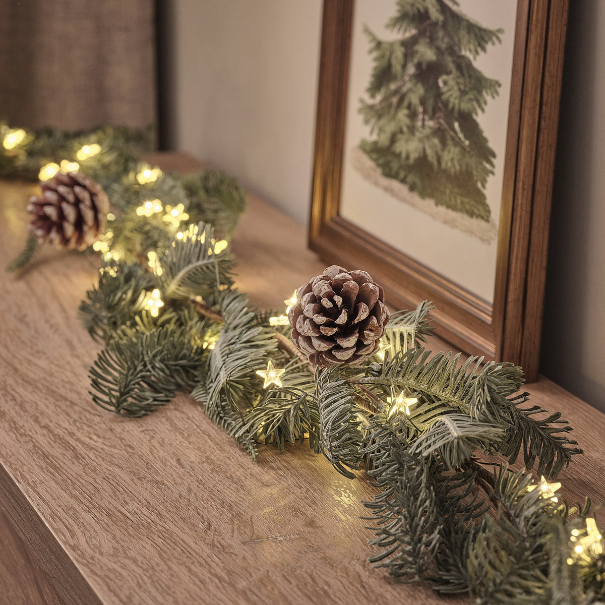 Nahaufnahme der beleuchteten Weihnachtsgirlande mit Tannenzapfen auf Holzfläche vor Bild