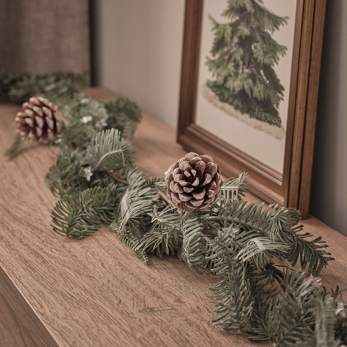 Detailansicht der beleuchteten Weihnachtsgirlande mit Tannenzapfen auf Holzfläche