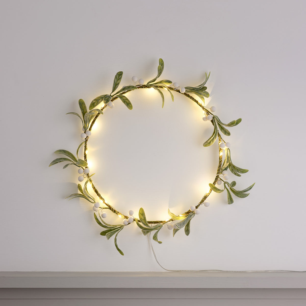 Minimalistischer LED-Mistelzweig-Kranz mit weißen Beeren und warmweißen Lichtern an weißer Wand