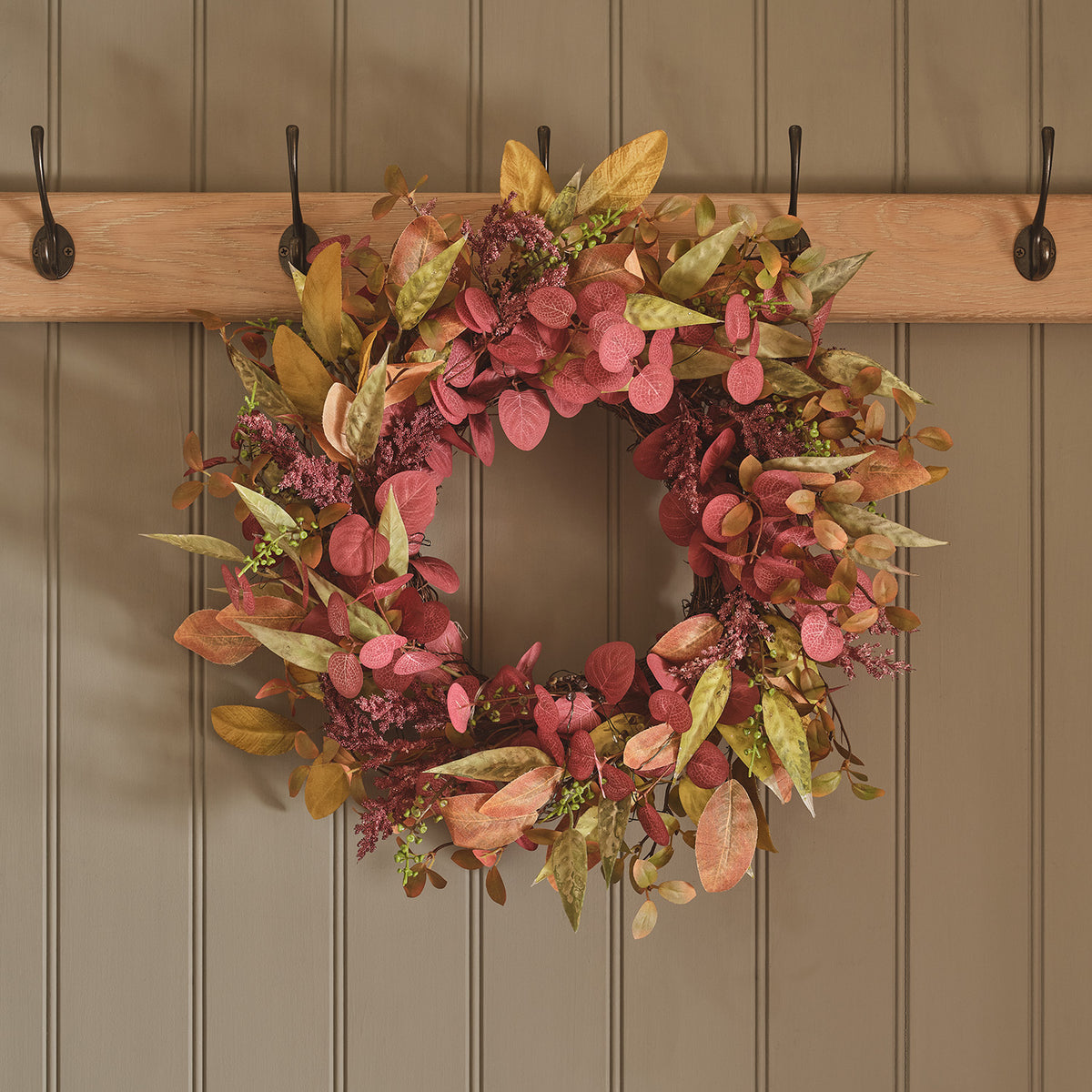 Herbstkranz mit künstlichen Blättern in Rot- und Grüntönen und warmweißen LEDs an einer Wand mit Haken