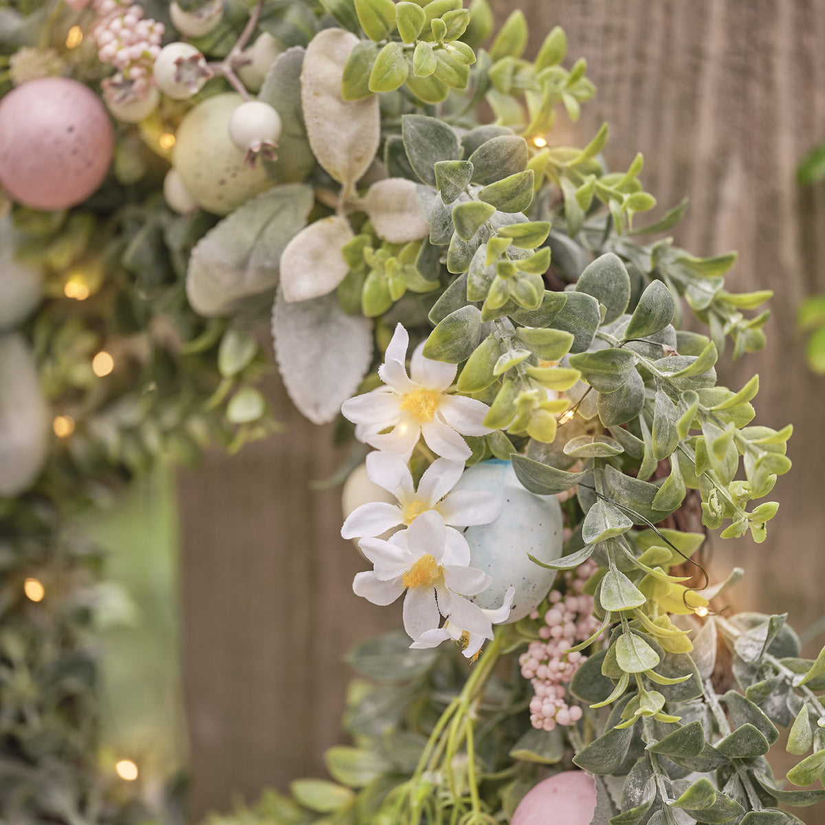 Nahaufnahme des Osterkranzes mit weißen Blüten, grünen Blättern und pastellfarbenen Eiern mit LED-Lichtern