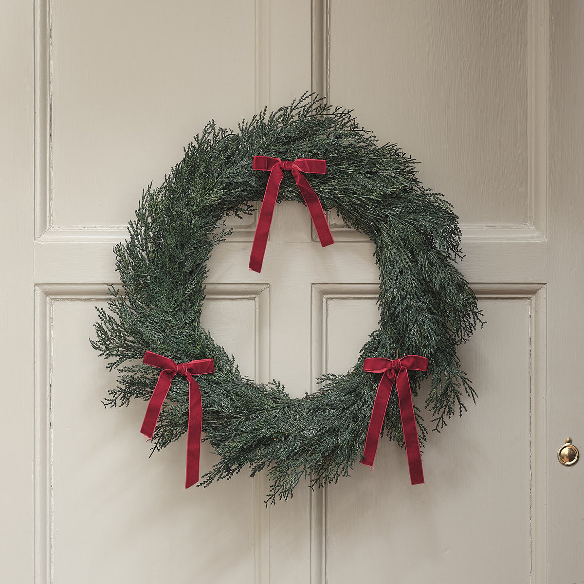 Weihnachtskranz mit roten Schleifen ohne Beleuchtung an weißer Haustür