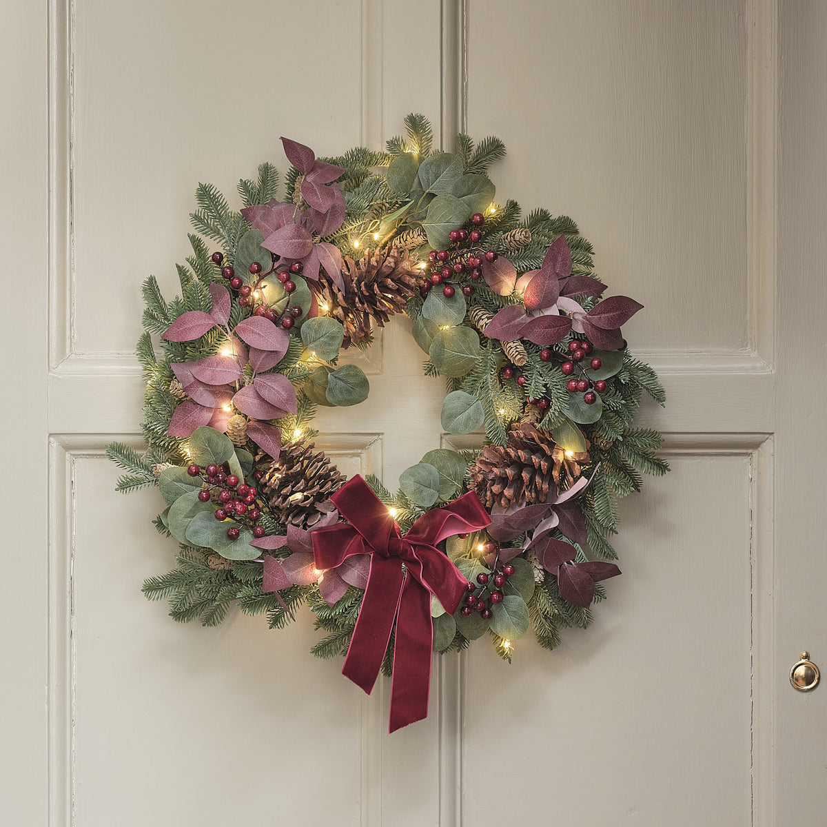 Weihnachtskranz mit warmweißen LEDs, Tannenzapfen, roten Beeren und Schleife an Tür