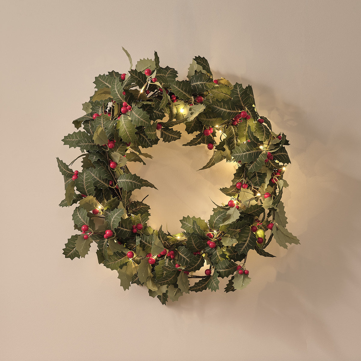 Nahaufnahme beleuchteter Weihnachtskranz mit Stechpalmenblättern und roten Beeren an Wand