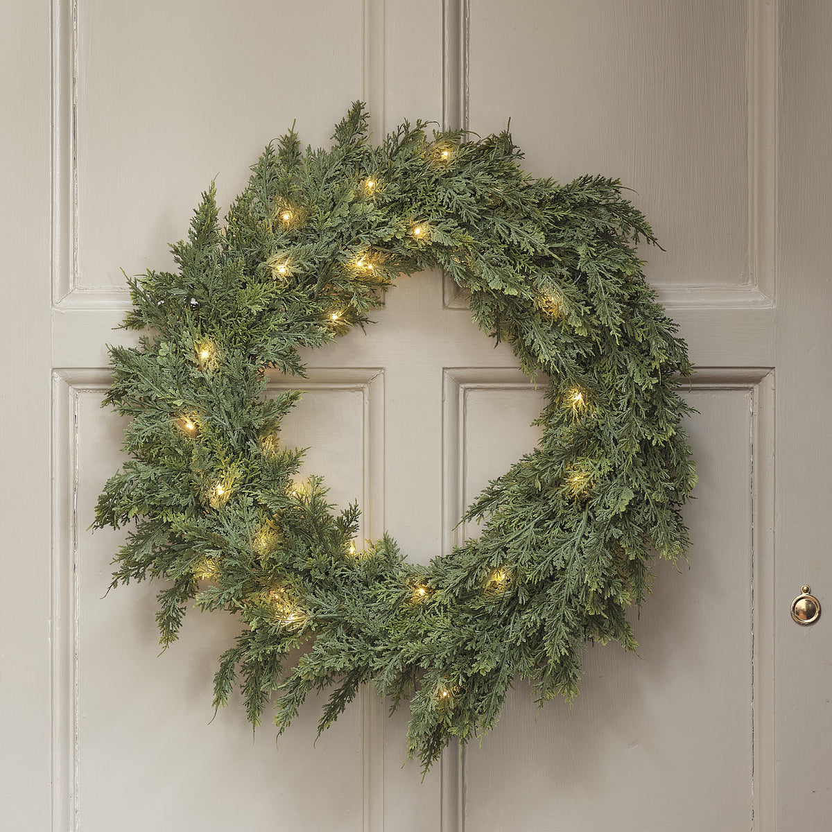 Grüner Weihnachtskranz mit warmweißen LEDs an cremefarbener Tür mit Türklopfer