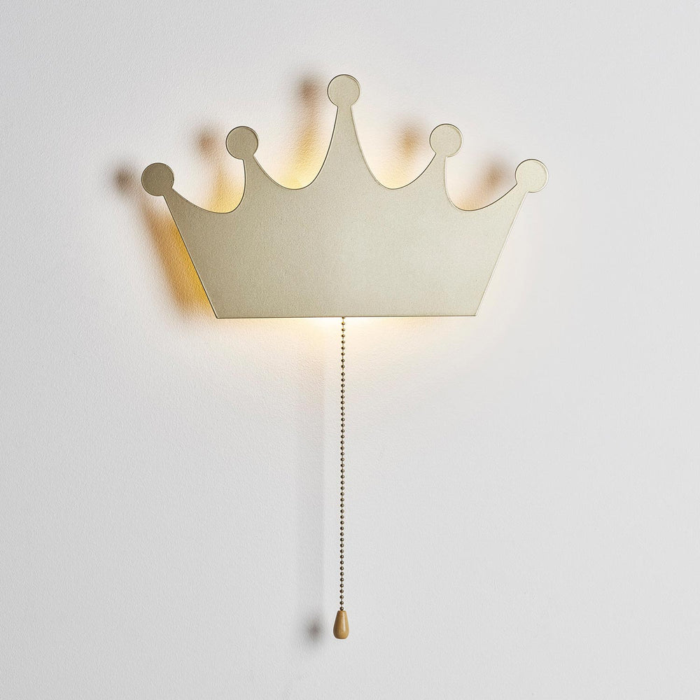 Goldene Metall-Krone als Wandlampe mit sanftem LED-Hintergrundlicht an weißer Wand