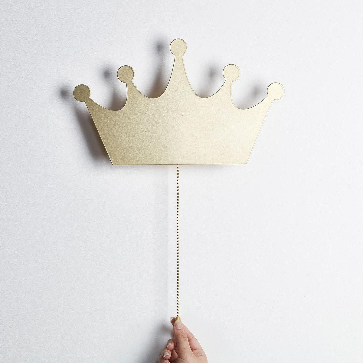 Goldene Kronen-Wandlampe mit Zugkette, Hand zieht an Kette zum Einschalten