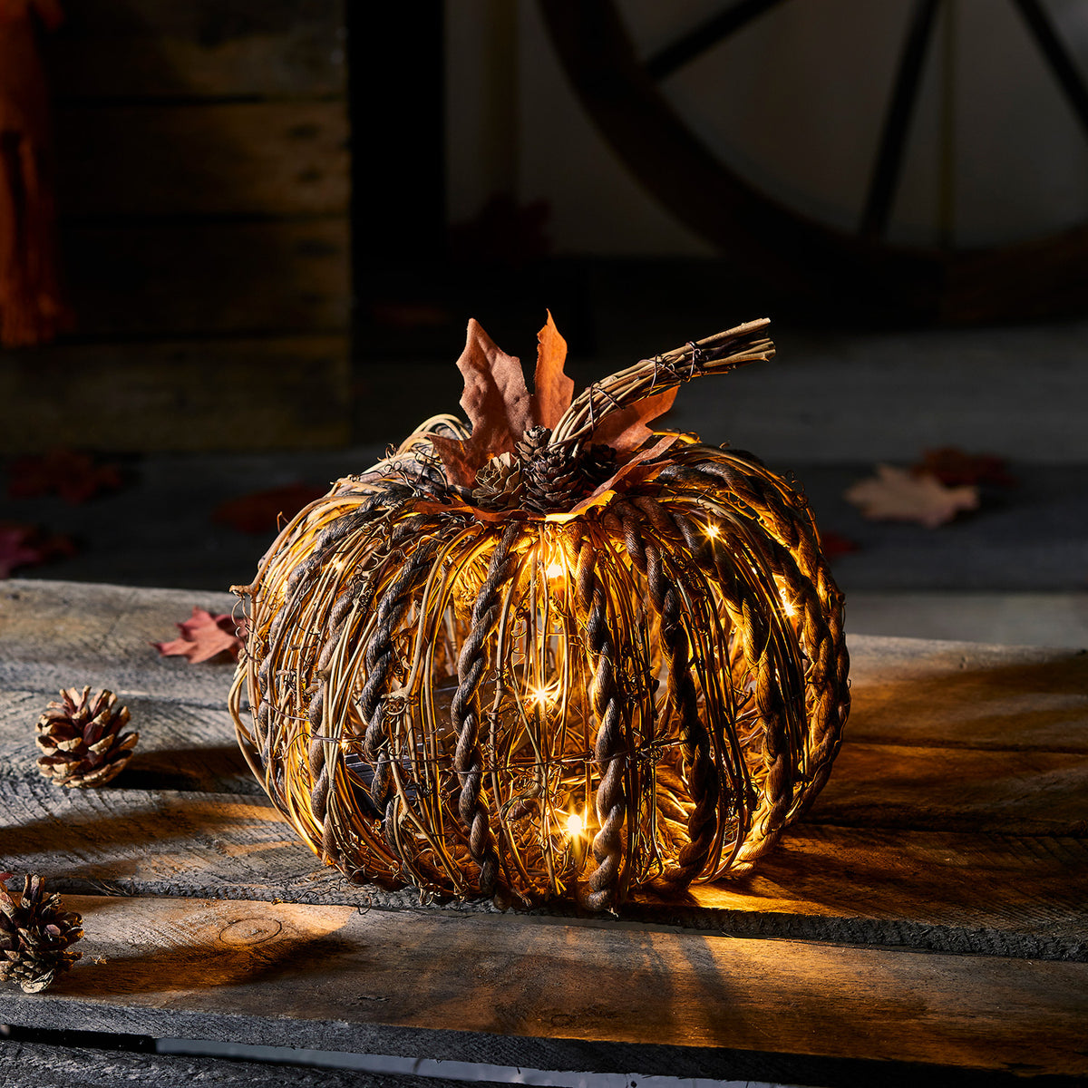 Beleuchteter Rattan-Kürbis mit LED-Lichtern und Herbstblättern auf dunklem Holztisch