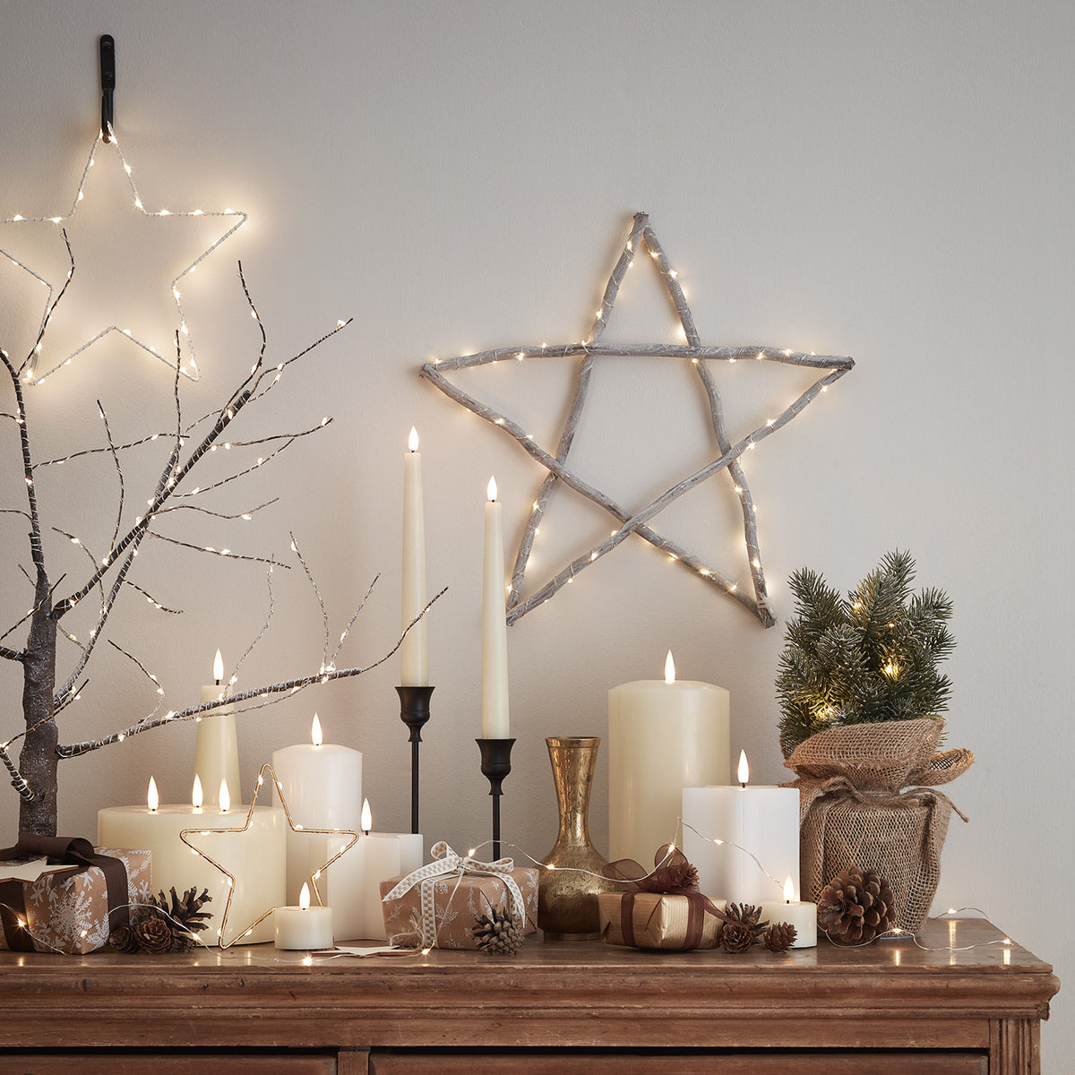 Weihnachtliche Dekoration mit beleuchtetem Holzstern, Kerzen und Geschenken auf Kommode