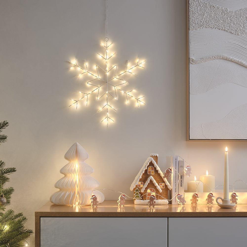 LED-Schneeflocke an Wand über Sideboard mit Weihnachtsdeko und Kerzen