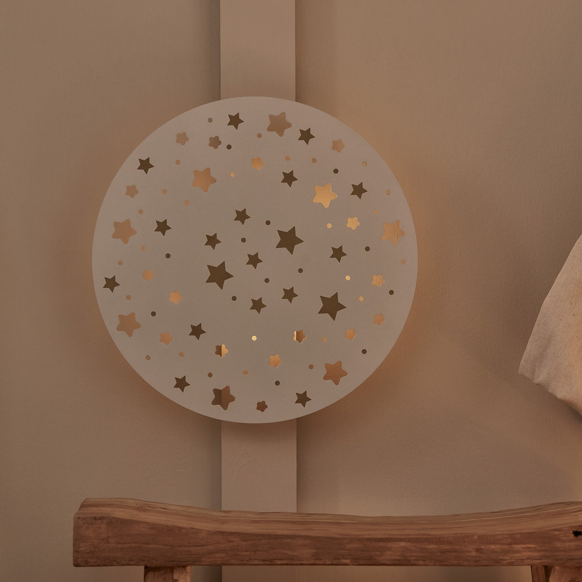 Wandleuchte mit Sternenausschnitten ohne Beleuchtung an Wand über Holzbänkchen