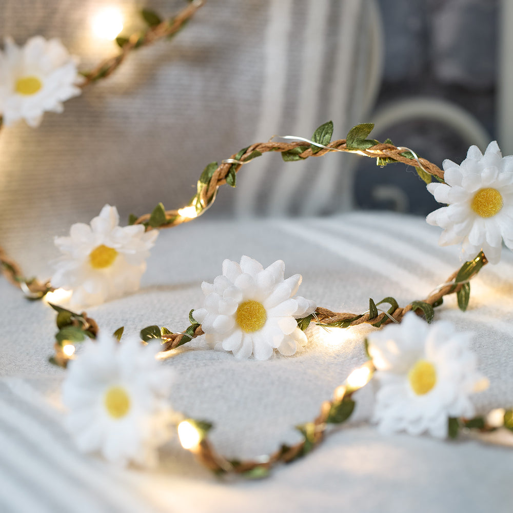 Nahaufnahme der LED-Girlande mit weißen Stoff-Gänseblümchen und warmweißen Lichtern auf hellem Stoff