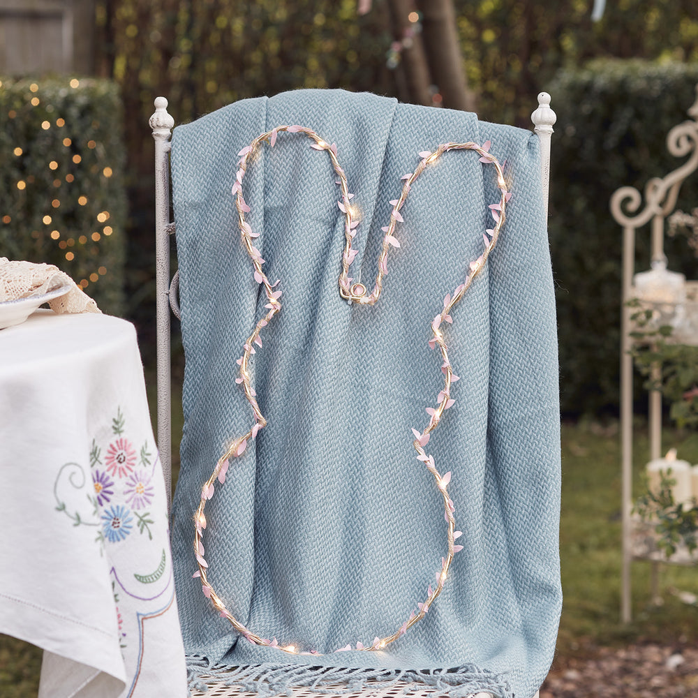 Hasenkranz mit Micro-LEDs und rosa Blüten auf blauem Strickstoff auf Stuhl drapiert