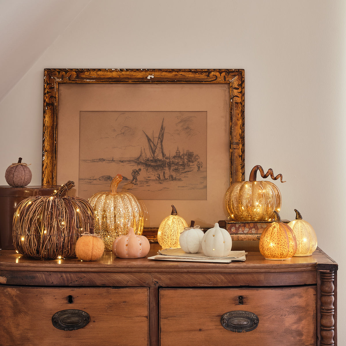 Herbstliche Dekoration mit Rattan- und Glas-Kürbissen auf antiker Kommode