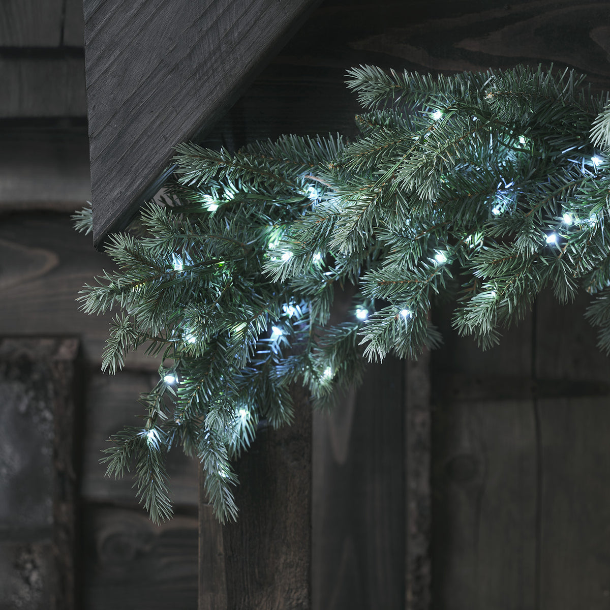 Nahaufnahme der Tannengirlande mit weißen LED-Lichtern an dunklem Holz