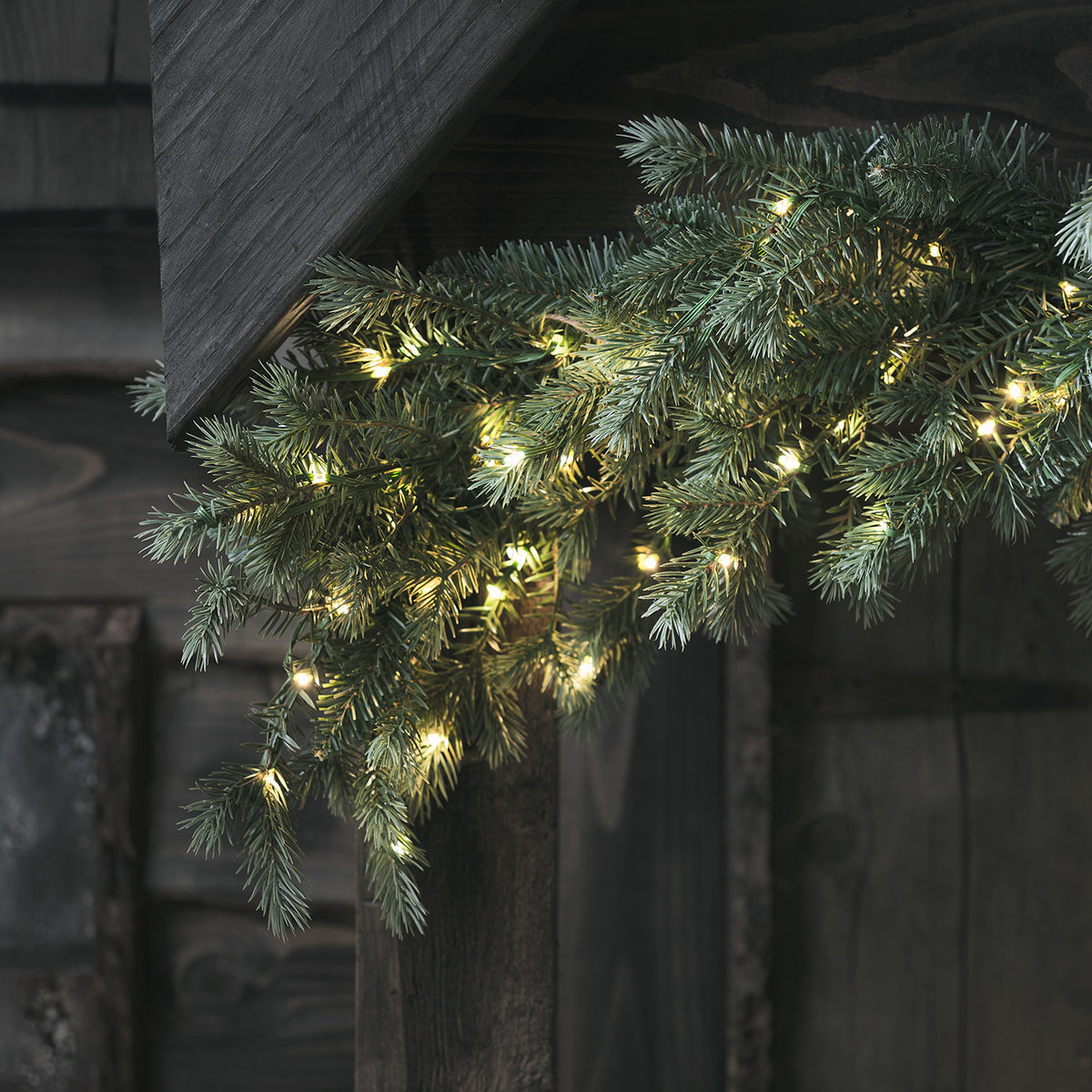 Künstliche Tannengirlande mit warmweißen LED-Lichtern an dunklem Holz