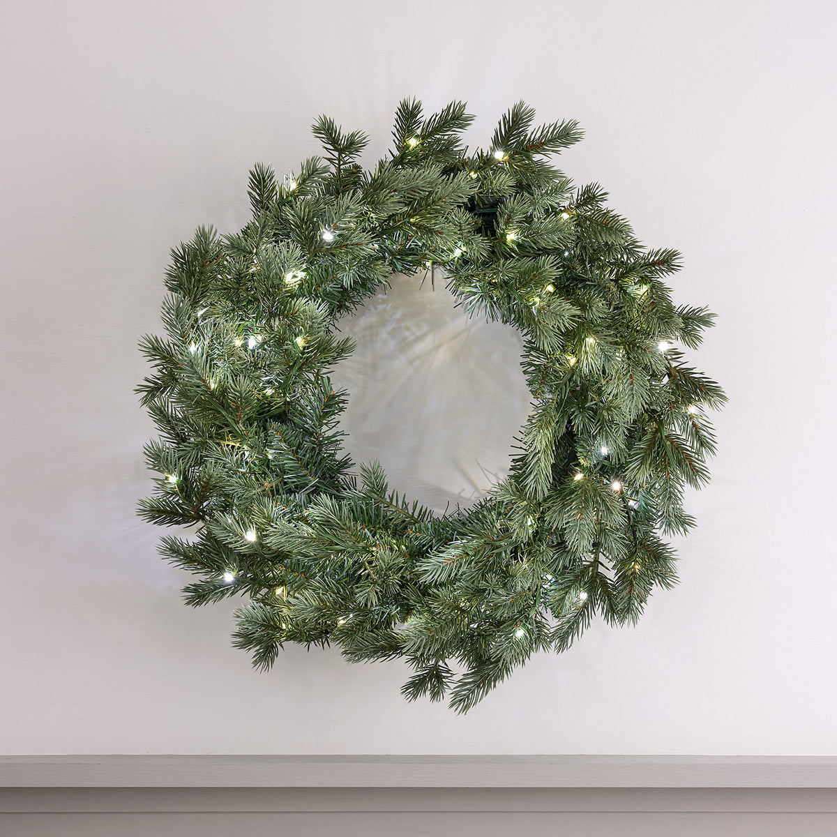 Weihnachtskranz mit kaltweißen LEDs an weißer Wand hängend
