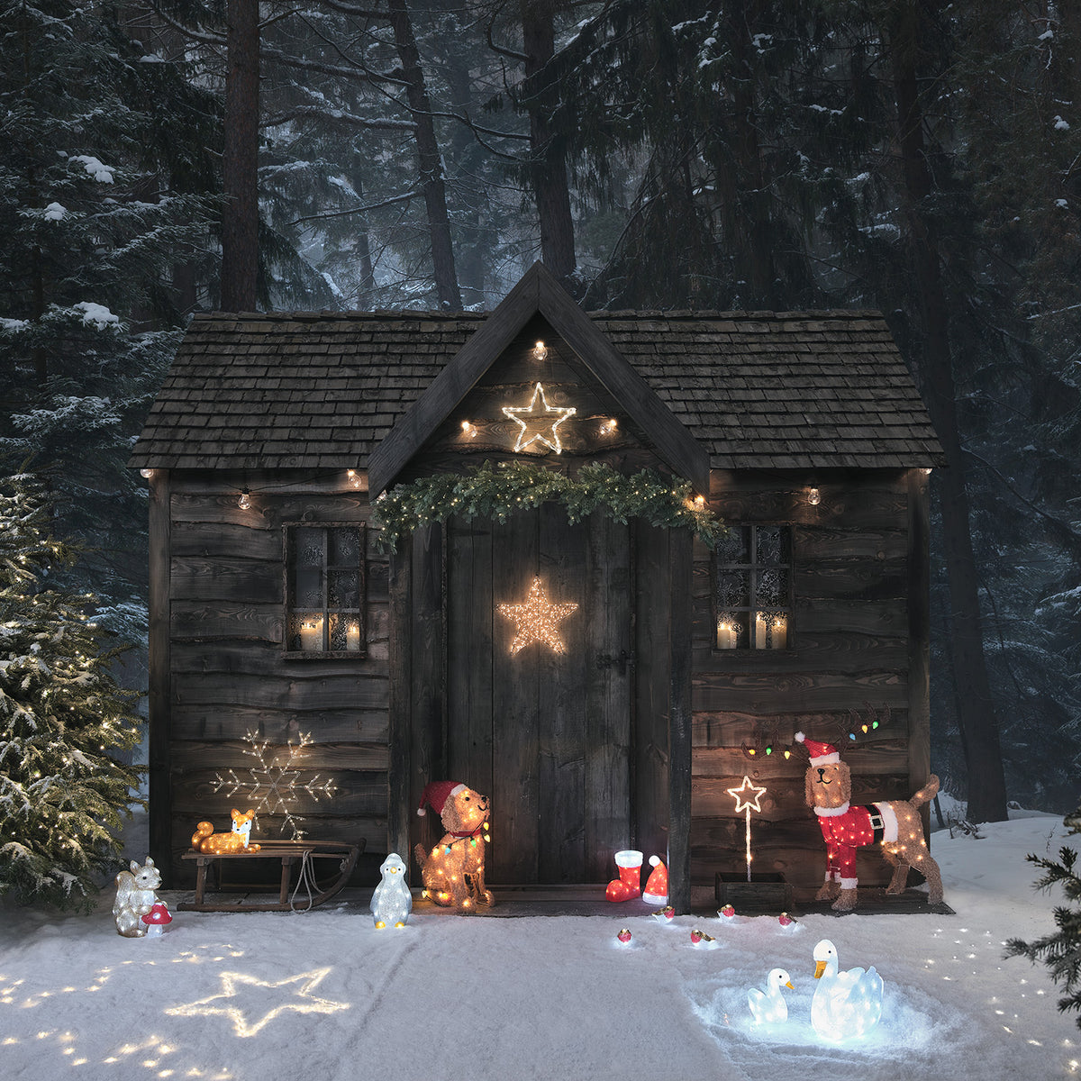 Weihnachtlich beleuchtete Holzhütte mit verschiedenen LED-Figuren im verschneiten Wald
