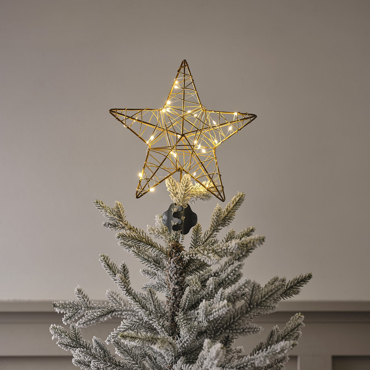 Goldener Metallstern mit eingeschalteten warmweißen LED-Lichtern als Weihnachtsbaumspitze auf künstlichem Tannenzweig