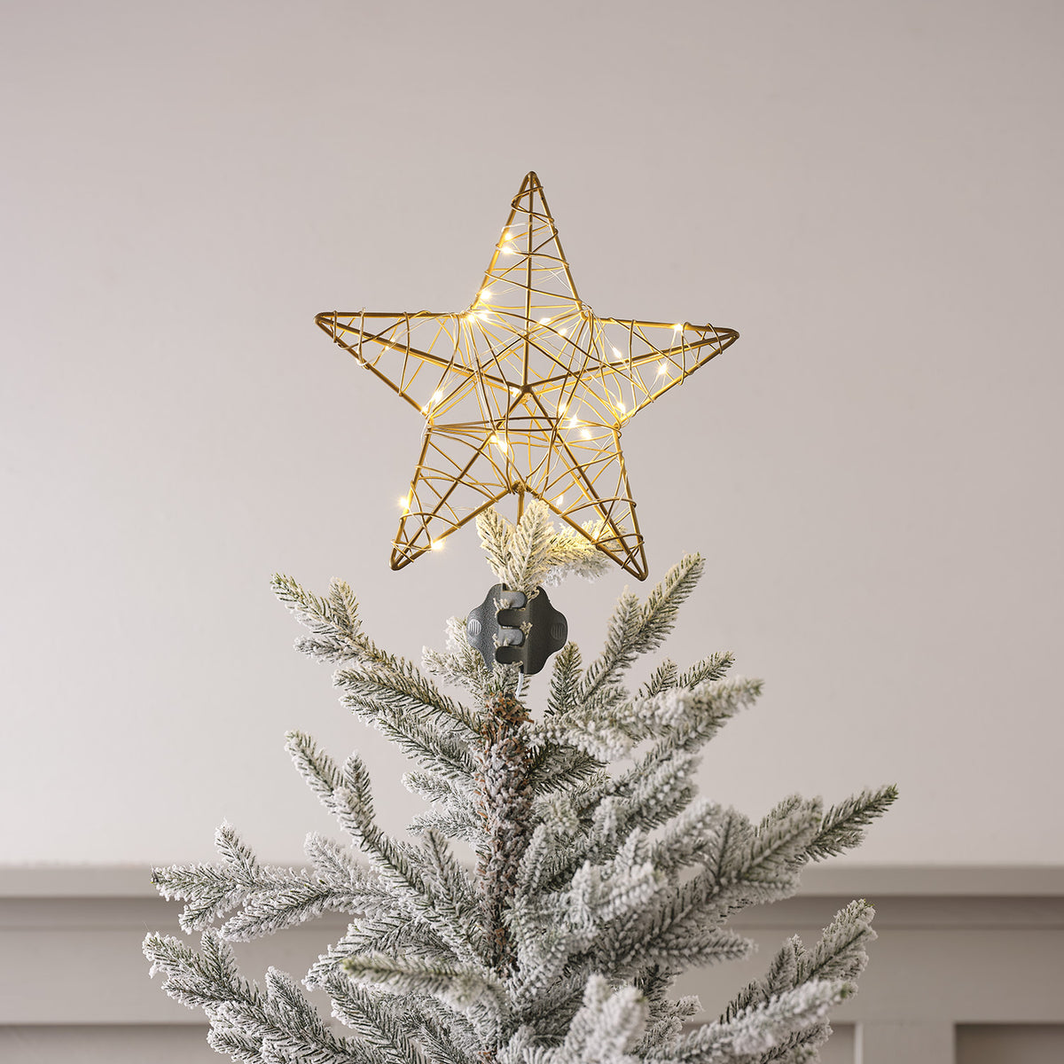 Goldener Metallstern mit warmweißen LED-Lichtern als Weihnachtsbaumspitze auf künstlichem Tannenzweig