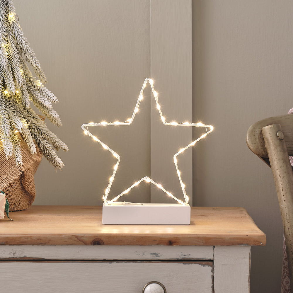 Weiße LED Stern Tischleuchte auf Holzkommode neben dekoriertem Tannenzweig