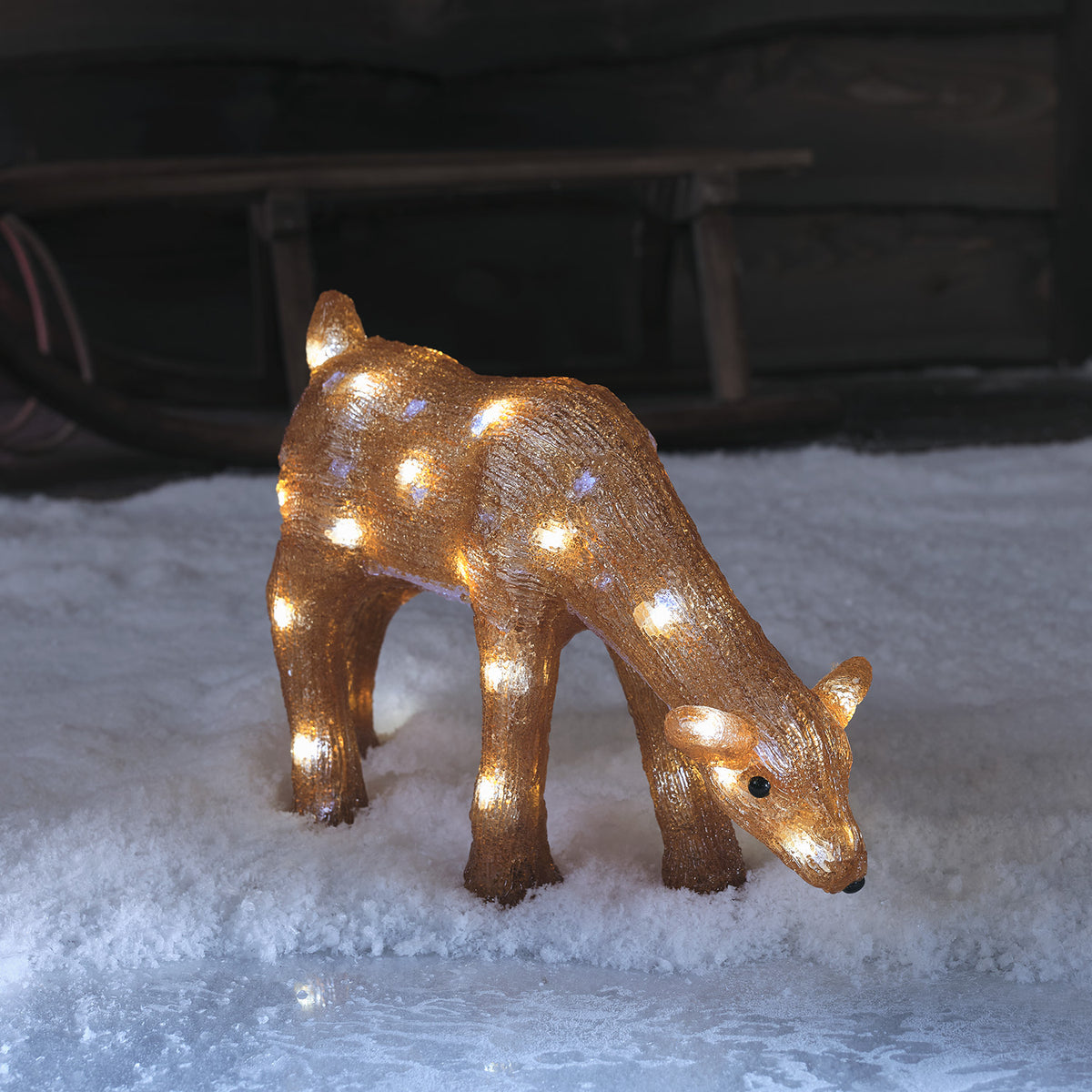 Leuchtende Acrylfigur eines grasenden Rentier Hirschkuhs mit weißen LED-Lichtern im Schnee