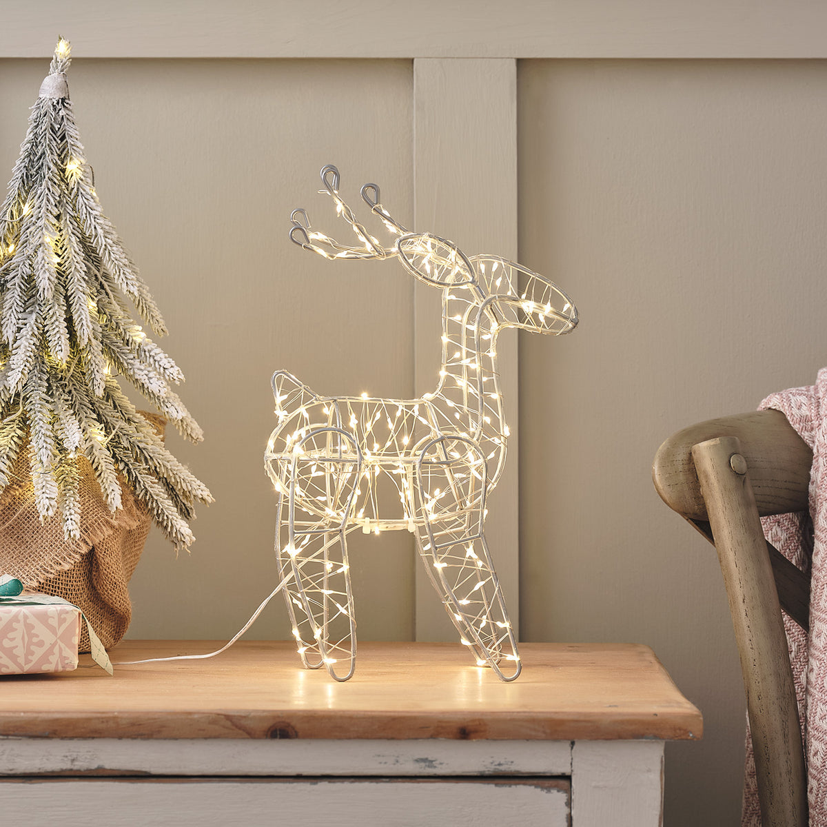 Batteriebetriebenes Mikro-LED-Rentier mit warmweißen Lichtern auf einem Holztisch neben einem kleinen Weihnachtsbaum