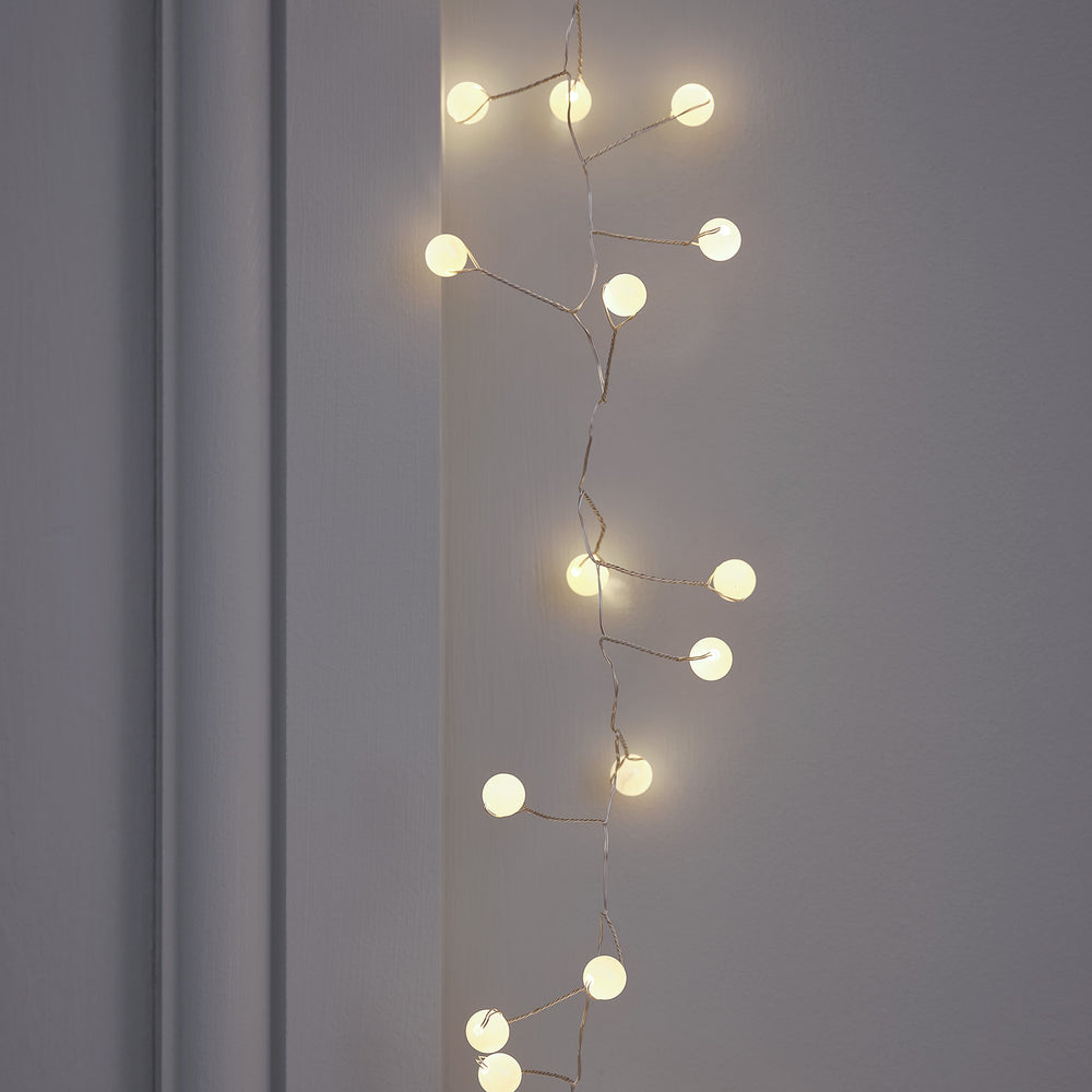 Perlencluster Lichterkette mit warmweißen Kugeln an grauer Wand hängend