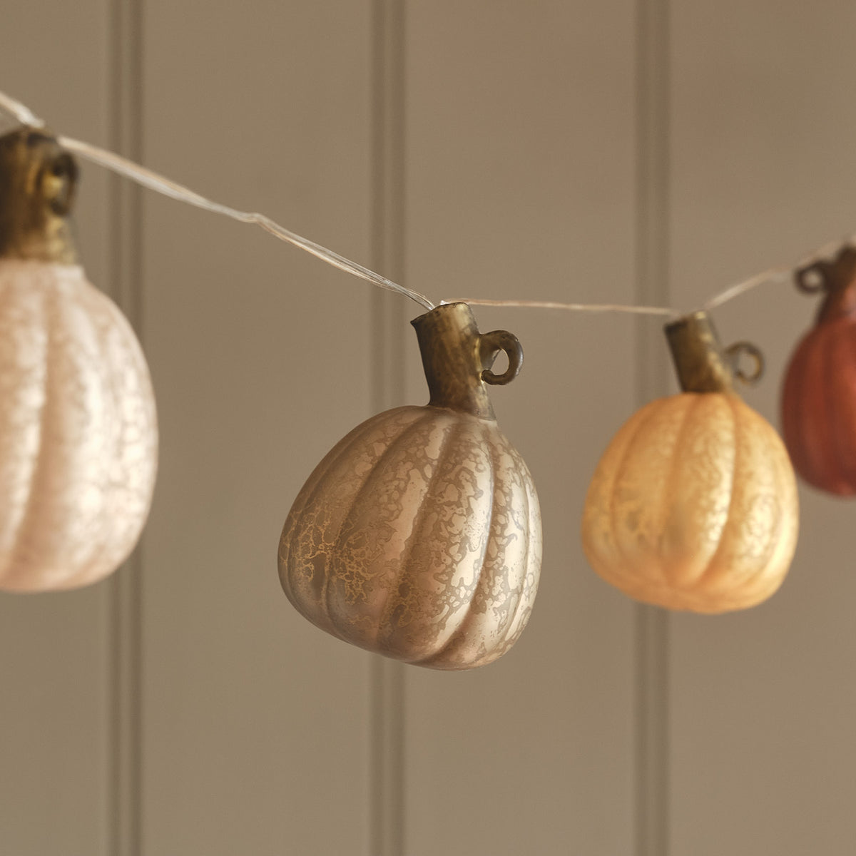Detailaufnahme von mehreren Kürbissen aus Glas an LED Lichterkette in Herbstfarben